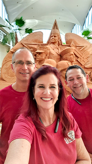 Sand sculptors Koet, Jill Harris and Woodworth pose in front of one of their sand sculptures under construction.