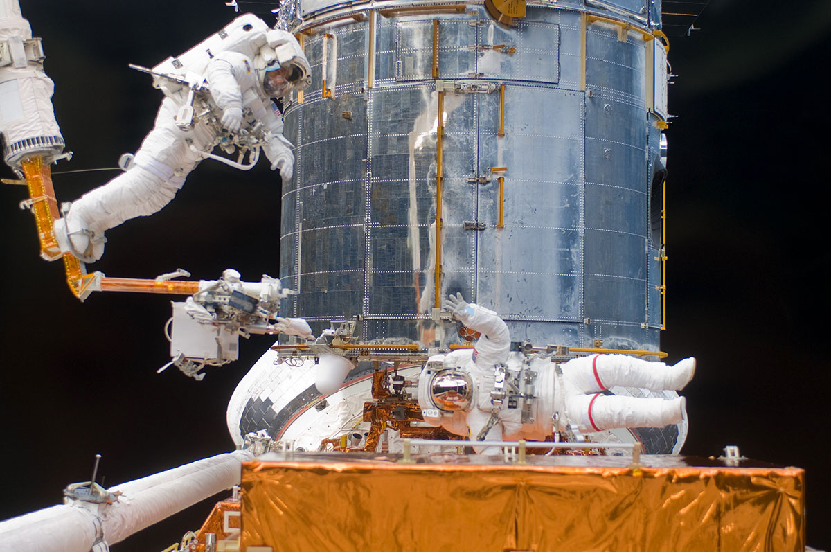 Mission specialist Andrew Feustel navigates near the Hubble on the end of the remote manipulator system arm, in 2009. Astronaut John Grunsfeld signals to his crewmate.