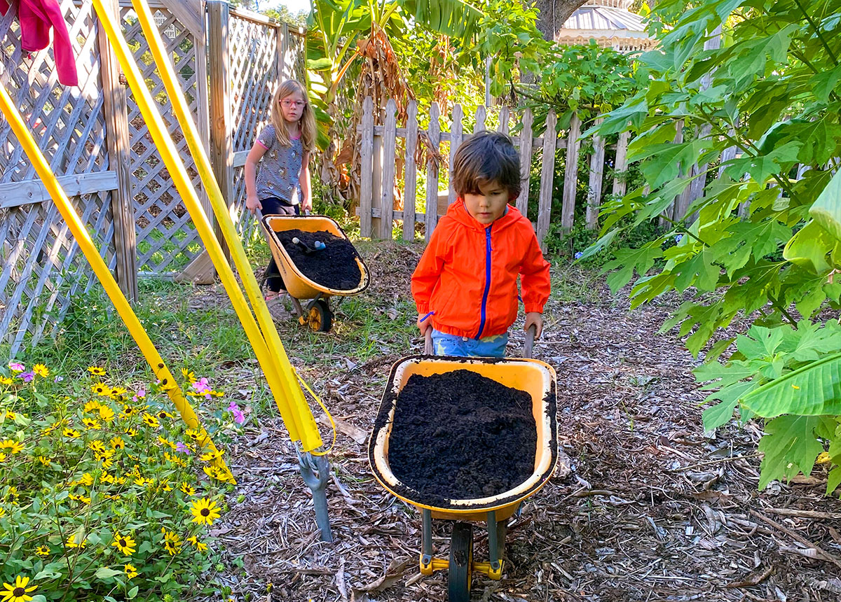Two young students move fresh soil to the garden at Verdi Ecoschool with the use of child-sized wheelbarrows.